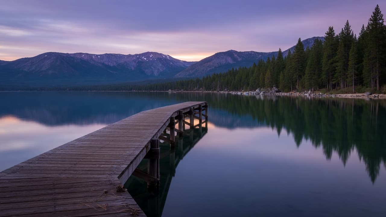 Wooden pier on calm Lake Tahoe water at dusk with mountain reflections